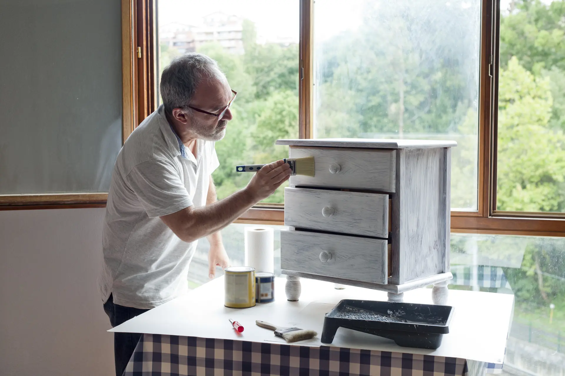 Peintre repeignant une commode en bois près d'une fenêtre