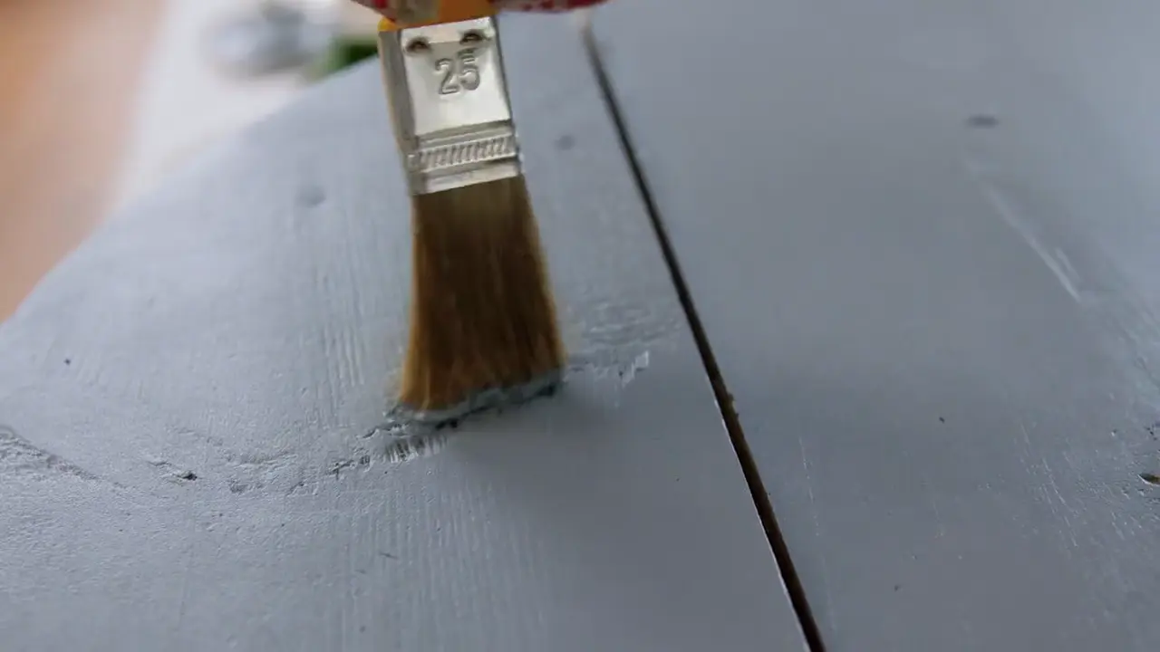 Pinceau appliquant une peinture grise sur du bois