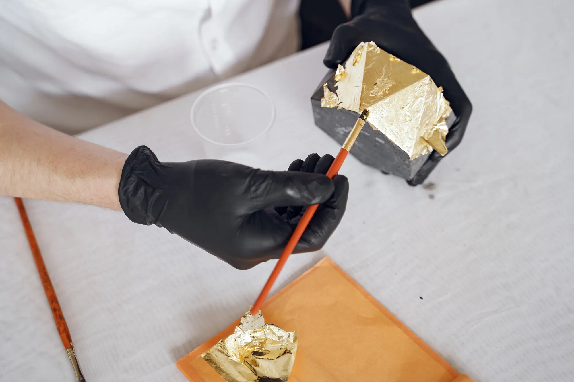Doreur appliquant une feuille d'or au pinceau avec des gants noirs